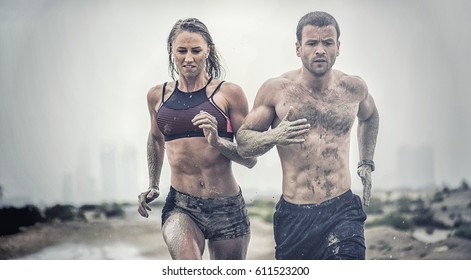 Muscular male and female athlete covered in mud running down a rough terrain with a desert background in an extreme sport race with grungy textured finish - Shutterstock ID 611523200