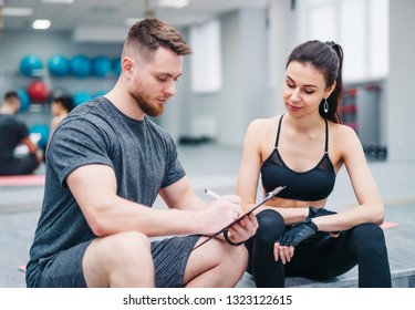 Muscular male instructor writing on a clipboard special workout for a pretty girl on the blurred background. Woman with personal trainer preparing training plan in gym - Powered by Shutterstock