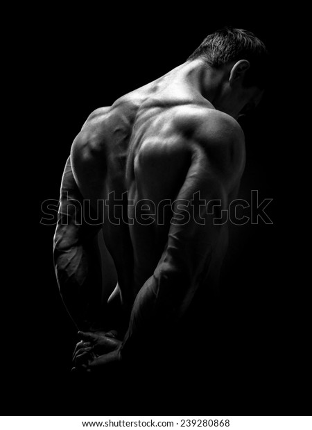 Muscular male model bodybuilder preparing for\
fitness training, turned back. Studio shot on black background.\
Black and white photo.