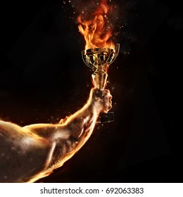 Muscular Man Arm Holding Burning Trophy Cup On Black Background. Detail Of Fighter Hand. Concept Of Success, Hard Work And Conquest Of The Target. High Resolution