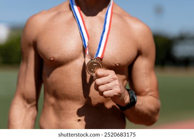 A muscular man athlete displays a gold medal, showcasing his achievement. Athletic male winner, with a fit physique, embodies success and dedication in sports, holding a gold medal. Winner in sports. - Powered by Shutterstock