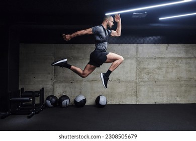 A muscular man captured in air as he jumps in a modern gym, showcasing his athleticism, power, and determination through a highintensity fitness routine - Shutterstock ID 2308505679