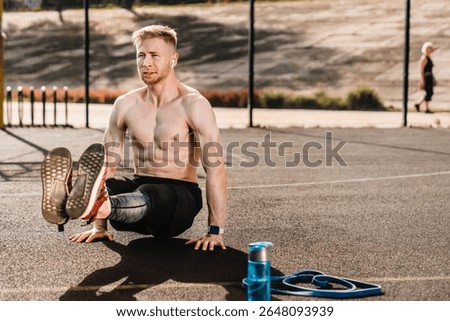 Muscular man does reverse push up exercise trains arms, keeps perfect body and good physical shape, has active workout outdoor, wears sport trousers and sneakers, poses on sport court