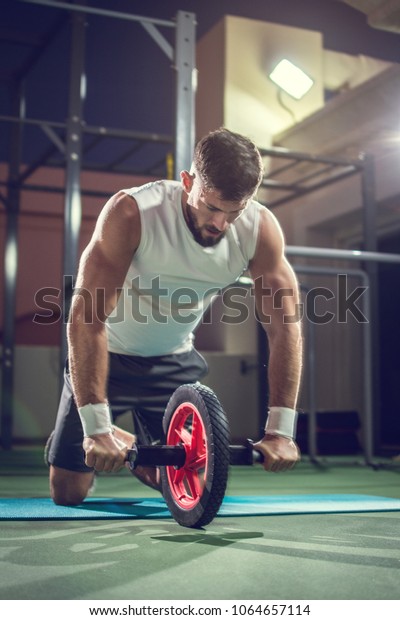 Muscular man doing exercises with abdominal toning\
wheel in gym