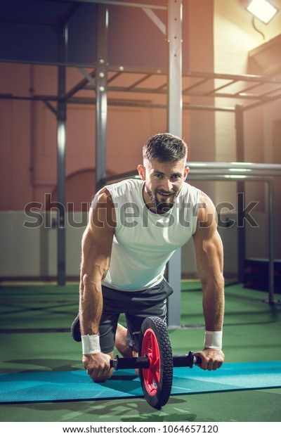 Muscular man doing exercises with abdominal toning\
wheel in gym