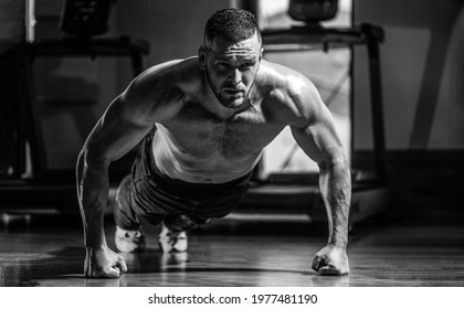 Muscular man doing push-ups on one hand against gym background. Man doing push-ups. Muscular and strong guy exercising. Slim man doing some push ups a the gym. Black and white.