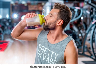 Muscular Man Drinking Sports Nutrition Sitting With Dumbbell In The Gym