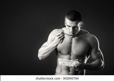 Muscular Man Eats Cottage Cheese On A Dark Background. Healthy Eating Professional Athlete. Delicious Food Full Of Vitamins. Photos For Sporting And Social Magazines, Posters And Websites.