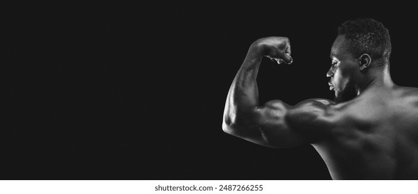 A muscular man flexes his bicep against a black background. - Powered by Shutterstock