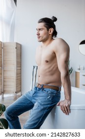 Muscular Man With Long Hair Sitting On Bathtub In Modern Bathroom