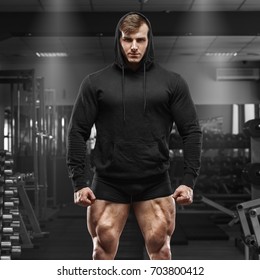 Muscular Man With Muscle Legs In Gym. Strong Male In Black Hoodie With Big Quads