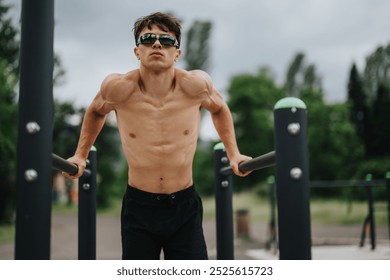 Muscular man performing a calisthenics workout on parallel bars outdoors. Fitness enthusiast exercising in a park setting, demonstrating strength and determination. - Powered by Shutterstock