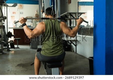 Muscular man performing lat pulldown workout, building back muscles and improving physical fitness in a gym environment