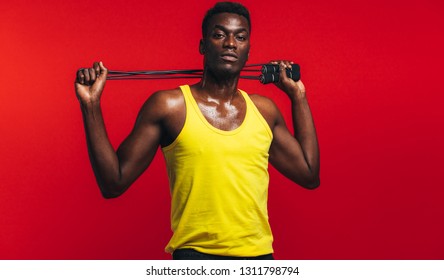 Muscular Man Posing With Jumping Rope On Red Background. African Fitness Model With Skipping Rope.