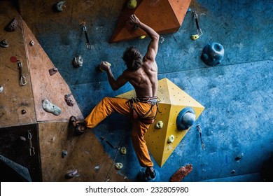 Muscular man practicing rock-climbing on a rock wall indoors  - Powered by Shutterstock