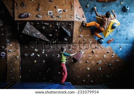 Muscular man practicing rock-climbing on a rock wall indoors 
