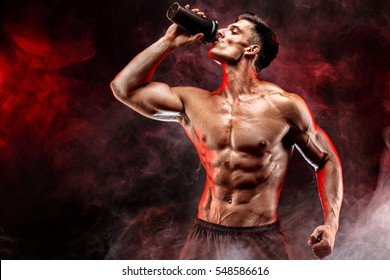 Muscular Man With Protein Drink In Shaker Over Dark Smoke Background