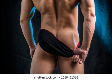 Muscular man pulling down underwear to show his butt, in studio shot