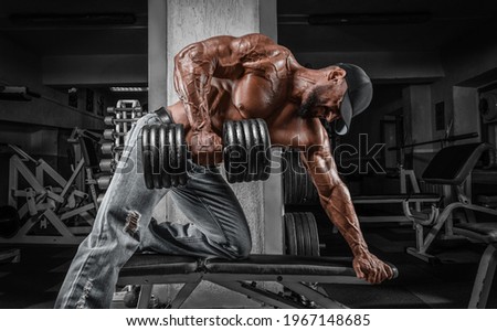 Muscular man pulls a dumbbell towards his stomach. Bodybuilding and powerlifting concept. Mixed media