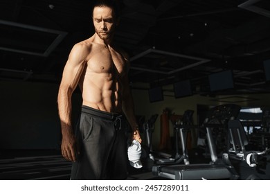 A muscular man, shirtless, standing in a gym setting, showcasing his physical strength and dedication to working out. - Powered by Shutterstock