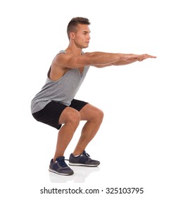 Muscular Man Showing A Squat Exercise, Side View. Full Length Studio Shot Isolated On White.