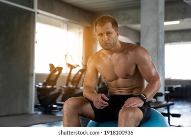 Muscular Man Sitting On Ball And Take A Break After His Workout In The Fitness Gym