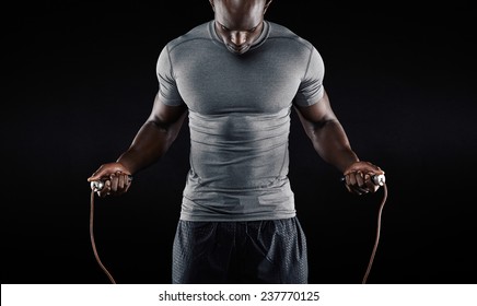 Muscular man skipping rope. Portrait of muscular young man exercising with jumping rope on black background