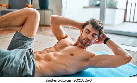 Muscular man in sports shorts doing a workout at home in a spacious living room. Healthy active lifestyle, sports, fitness.