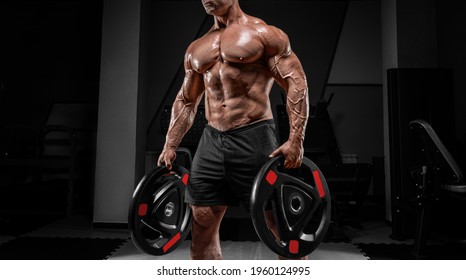 Muscular man stands in a gym with barbell discs. Bodybuilding and powerlifting concept. Mixed media