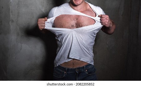 Muscular man tearing a white T-shirt to his chest with his hands.