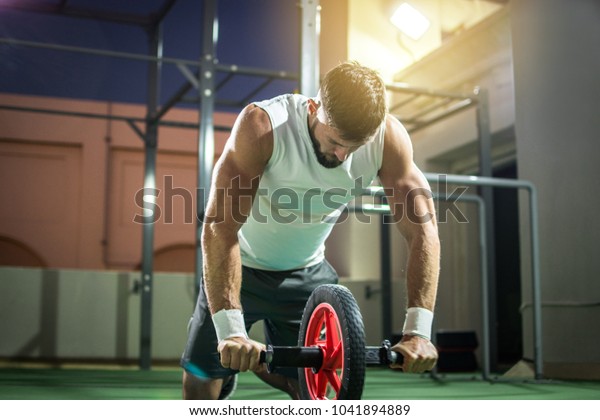 Muscular man training with abdominal toning\
wheel to strengthen his six-pack\
muscles.