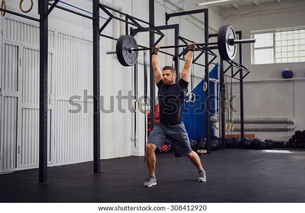Muscular man\
training lunges with barbells over\
head
