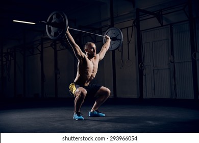 Muscular man training squats with barbells over head