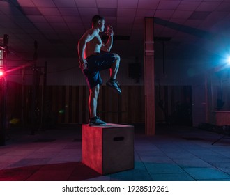 Muscular man training wooden box pacing in dark gym. Athlete workout in red blue neon light. Healthy lifestyle cross training