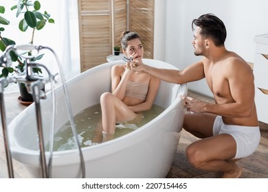 Muscular Man In Underpants Lighting Cigarette Of Girlfriend Relaxing In Bathtub