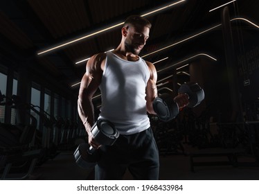 Muscular man in a white t-shirt works out in the gym with dumbbells. Biceps pumping. Fitness and bodybuilding concept. Mixed media