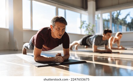 muscular man and woman doing planking exercises in gym on a yoga mat position on elbows while training in studio