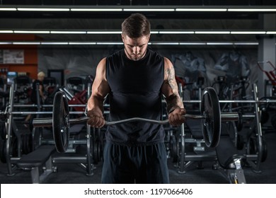 Muscular Man Working Out In Gym Doing Exercises With Barbell At Biceps