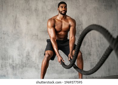 Muscular man working out on the battle ropes in a gym