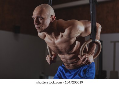 Muscular Mature Male Crossfit Athlete Doing Ring Dips, Copy Space. Shirtless Sportsman With Six Pack Perfect Abs Working Out On Gymnastic Rings At Crossfit Box Gym