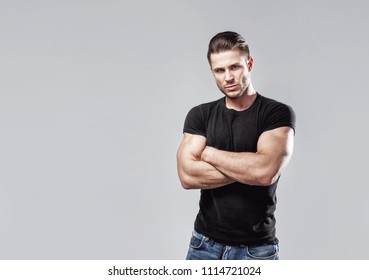 Muscular Model Sports Young Man In Jeans And Black T-shirt On A Grey Background. Fashion Portrait Of Brutal Sporty Healthy Strong Muscle
Guy With A Modern Trendy Hairstyle.