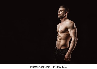 Muscular model sports young man on dark background. Fashion portrait of  strong brutal guy with a modern trendy hairstyle. Sexy torso. Male flexing his muscles. Sport workout bodybuilding concep. 