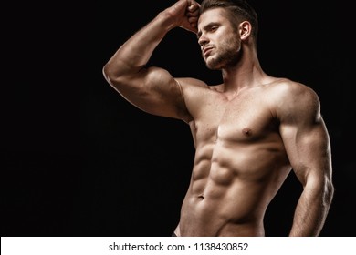 Muscular model sports young man on dark background. Fashion portrait of strong brutal guy with a modern trendy hairstyle. Sexy torso. Male flexing his muscles. Sport workout bodybuilding concep. 