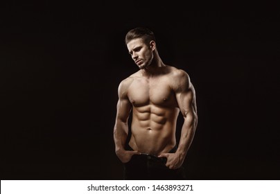 Muscular model sports young man on dark background. Fashion portrait of strong brutal guy with a modern trendy hairstyle. Sexy torso. Male flexing his muscles.