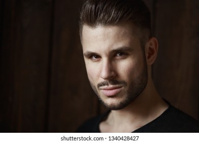Muscular model young man with beard in black t-shirt on dark wooden background. Fashion portrait of brutal sporty sexy strong muscle
guy with modern trendy hairstyle. Model, fashion concept.
