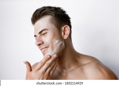 Muscular Sexy Model Sports Young Man On White Background. Portrait Of Beautiful Smiling Healthy Guy Applying Foam For Washing On His Face. Facial Skincare Routine.