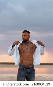 Muscular Sexy Young Man Taking Off T Shirt On Empty White Sand Beach And Turquoise Ocean. Sexy Summer Love.