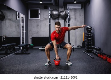 A muscular sportsman lifting kettle bell in a gym.