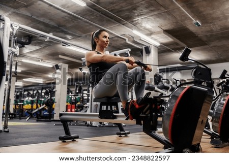A muscular sportswoman in shape is doing workouts on a rowing machine.