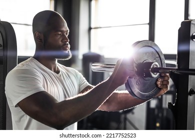 Muscular sporty african man adding weight on barbell at gym - Shutterstock ID 2217752523